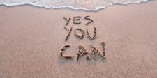 Words reading “Yes You Can” written in sand near the edge of the water.