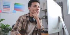 Upwork’s numbers explain why freelancers say the platform has changed Man with headphones around his neck looking thoughtfully at a desktop computer in a creative workspace.
