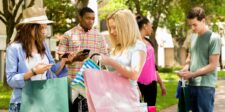 Group of people holding shopping bags and phones outdoors.