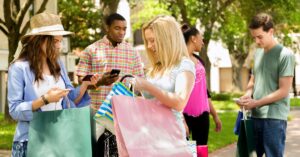 Group of people holding shopping bags and phones outdoors.