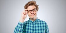 Man wearing glasses and a green plaid shirt looking toward the camera with a skeptical expression.