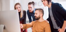 Team members gathered around a desktop computer while reviewing website work together.