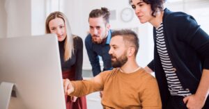 Team members gathered around a desktop computer while reviewing website work together.