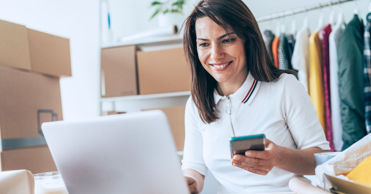 Woman using a laptop and smartphone while working in an online retail workspace.