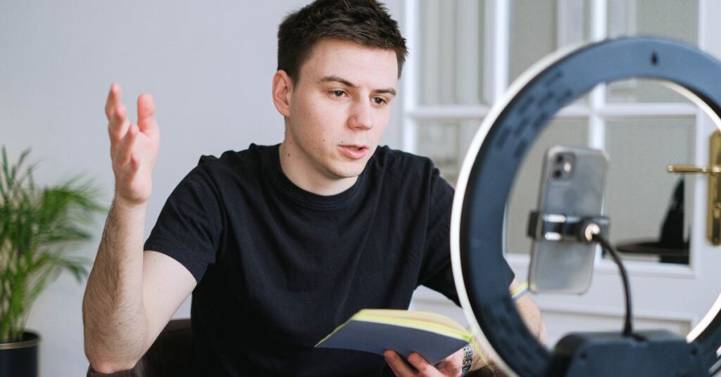 Creator filming a video with a smartphone and ring light while holding a notebook.