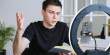 YouTube is making new creators work twice as hard before sharing ad revenue Creator filming a video with a smartphone and ring light while holding a notebook.