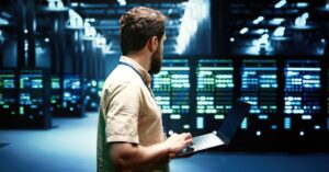 Technician working on a laptop inside a large data center with rows of server racks.