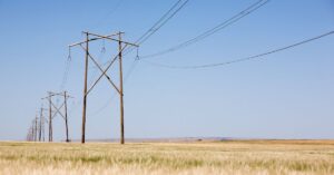 Power lines stretching across a prairie field under a clear blue sky.