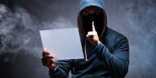 Masked hooded person holding a blank sign against a dark smoky background.