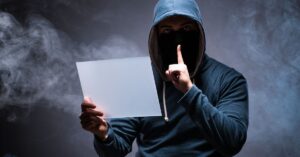 Masked hooded person holding a blank sign against a dark smoky background.