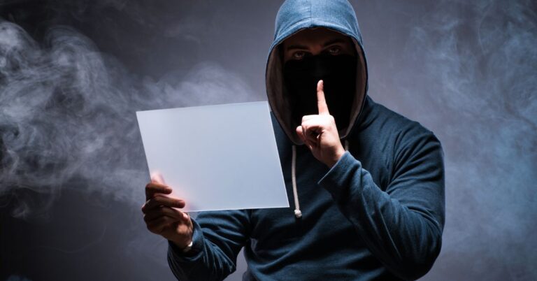Masked hooded person holding a blank sign against a dark smoky background.