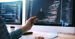 Developer reviewing code across multiple computer screens during a website security investigation.