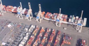 Aerial view of Roberts Bank Superport in British Columbia, showing a container ship, cranes, and rows of shipping containers.
