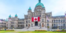British Columbia Parliament Buildings in Victoria with a large Canadian flag displayed above the entrance.