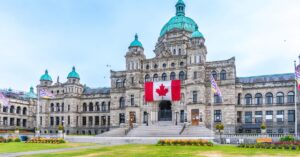 British Columbia Parliament Buildings in Victoria with a large Canadian flag displayed above the entrance.