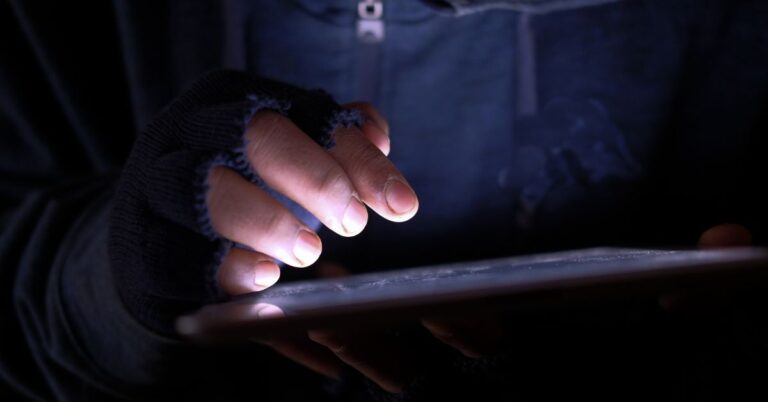 Close-up of a person using a tablet in a dark setting, representing a cybersecurity threat or active exploit.