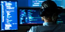 Person wearing headphones working at multiple monitors displaying code.