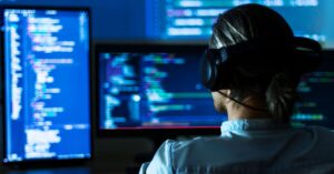 Person wearing headphones working at multiple monitors displaying code.