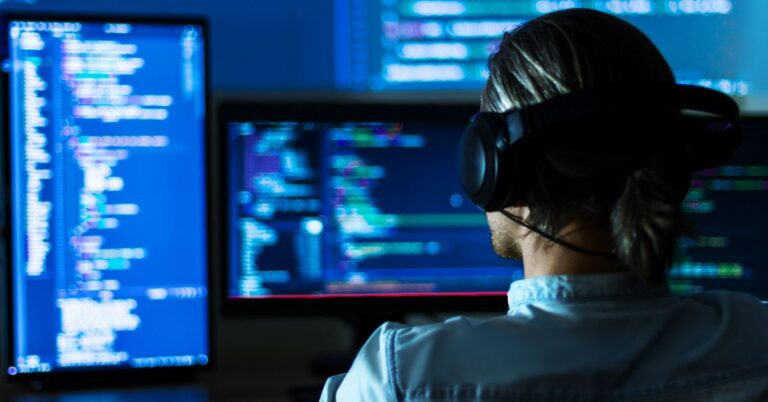 Person wearing headphones working at multiple monitors displaying code.