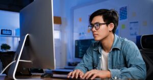 Web professional working at a desktop computer in a blue-lit office.