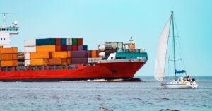 Container ship carrying stacked cargo containers sailing alongside a smaller sailboat.