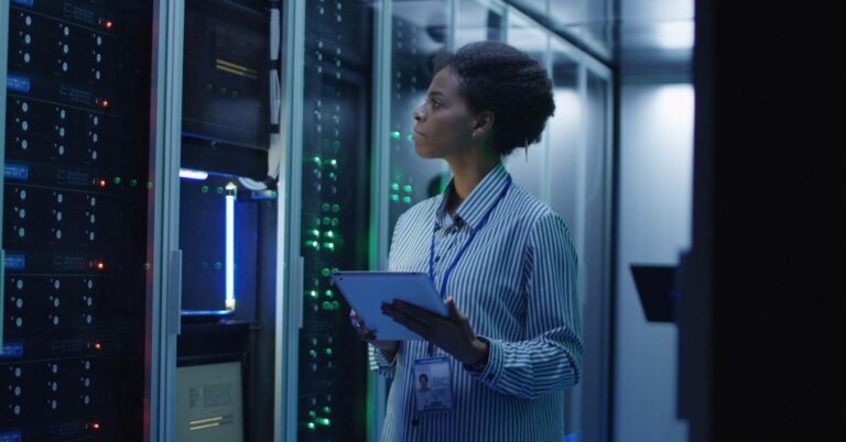 Data centre technician monitoring server infrastructure with a tablet.