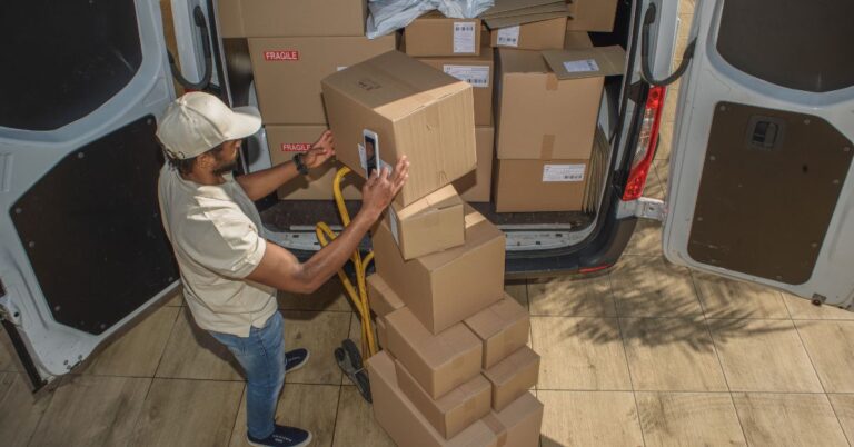 Delivery worker scanning packages beside a van loaded with cardboard parcels.
