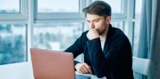 Man reviewing information on a laptop in a bright office.
