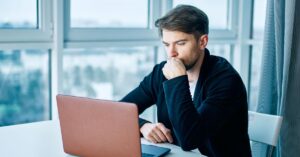 Man reviewing information on a laptop in a bright office.