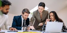 Guest post outreach: how to earn replies from sites worth pitching Four business professionals collaborating around a laptop and documents during a meeting.