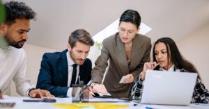Four business professionals collaborating around a laptop and documents during a meeting.