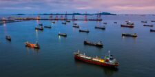Low Hormuz traffic puts freight, insurance and fuel costs back on watch Aerial view of multiple cargo and tanker ships near a busy port at dusk.