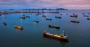 Aerial view of multiple cargo and tanker ships near a busy port at dusk.