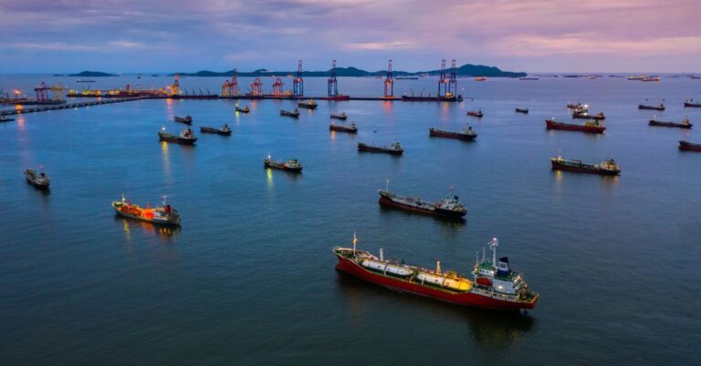Aerial view of multiple cargo and tanker ships near a busy port at dusk.