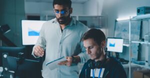 Two technology professionals reviewing computer systems and data in an office.