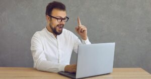 Man at a laptop raising one finger as if he has an idea.