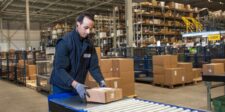 Holiday shipping costs are moving from forecast to invoice Warehouse worker handling parcels on a conveyor in a busy fulfilment centre.