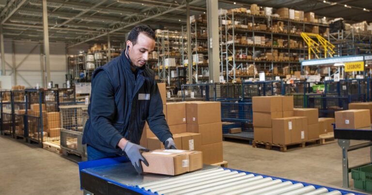 Warehouse worker handling parcels on a conveyor in a busy fulfilment centre.