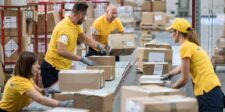 Warehouse workers sorting and scanning boxed inventory on a conveyor system.
