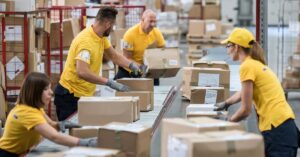 Warehouse workers sorting and scanning boxed inventory on a conveyor system.