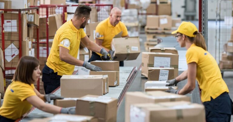Warehouse workers sorting and scanning boxed inventory on a conveyor system.