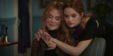 Two red-haired women sitting closely together and holding hands in a dimly lit room.