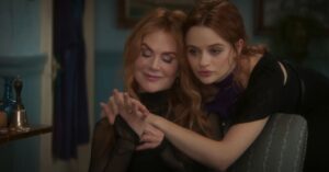 Two red-haired women sitting closely together and holding hands in a dimly lit room.