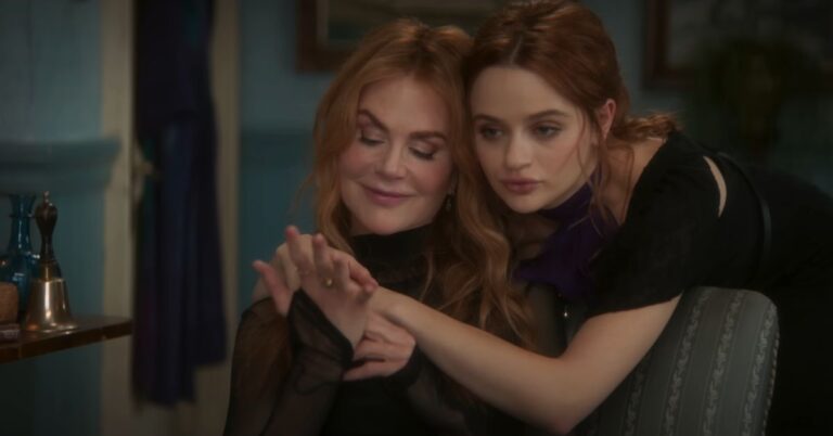 Two red-haired women sitting closely together and holding hands in a dimly lit room.
