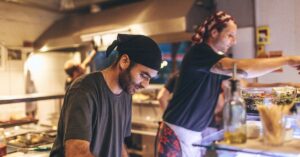 Restaurant workers preparing food behind the counter in a busy kitchen.