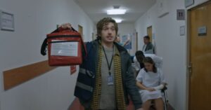 Medical courier carrying a red delivery bag through a hospital hallway in a scene from Resident Evil.