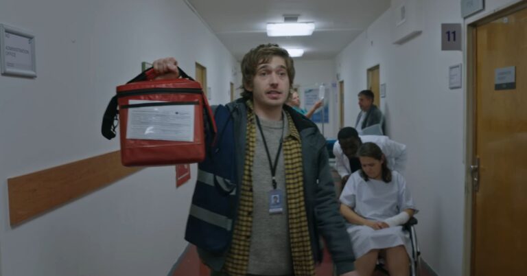 Medical courier carrying a red delivery bag through a hospital hallway in a scene from Resident Evil.