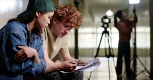 Film production team reviewing a script on set with a camera in the background.