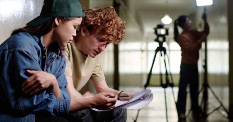 Film production team reviewing a script on set with a camera in the background.