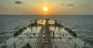 View across the deck of a crude oil tanker traveling at sea at sunset.